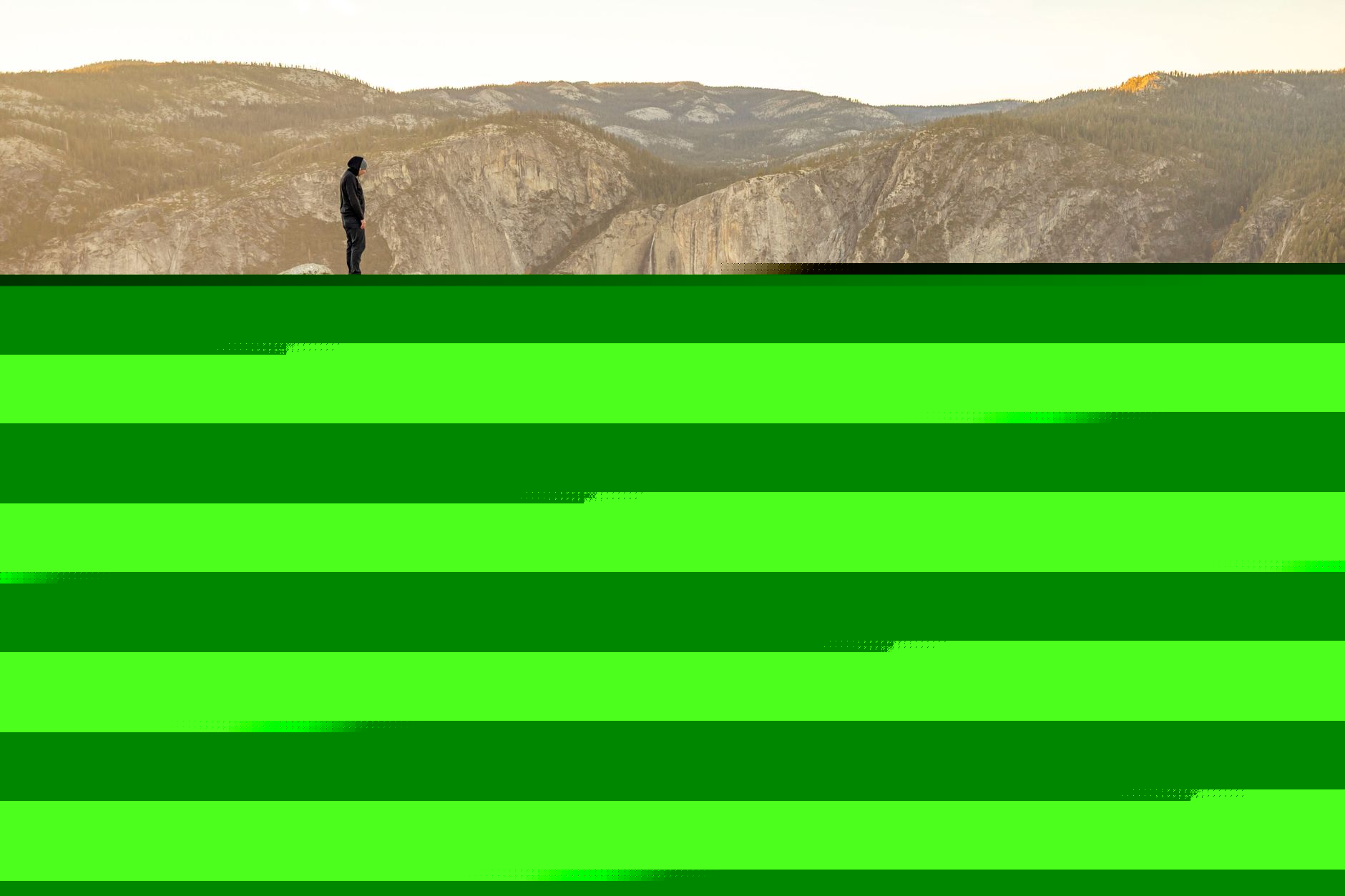 A hiker in a windbreaker on an exposed granite ridge with autumn foliage far below