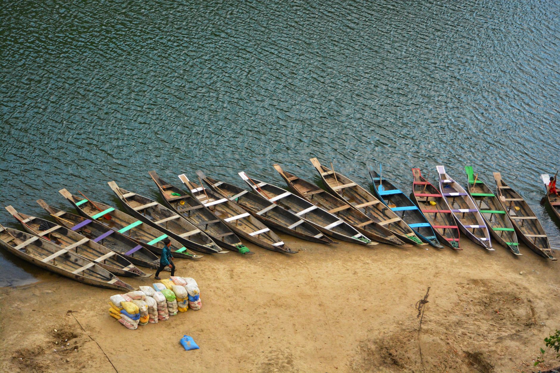 A loaded aluminum canoe on a lake shore, duffels and dry bags stacked beside it
