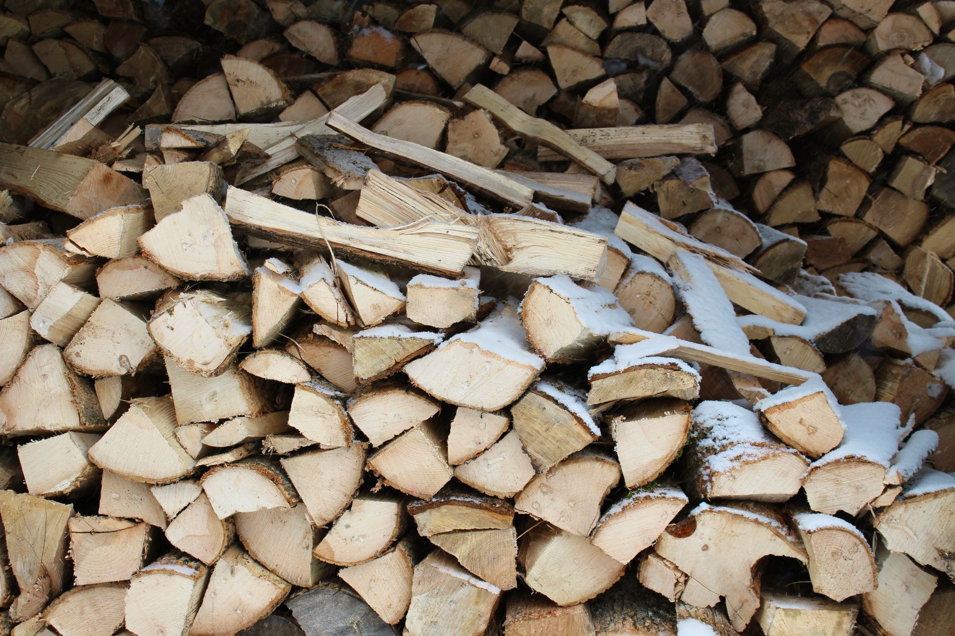 A stacked cord of split firewood next to a woodshed in the snow